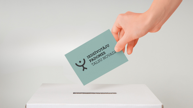 Rokā tiek turēta gaiši zila kartīte ar uzrakstu “Iedzīvotāju padomes Talsu novadā”, ko ievieto baltā balsošanas kastē.