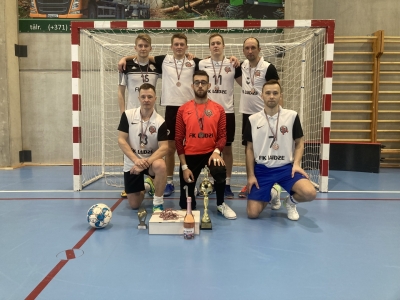 Futbola komanda zālē, baltos sporta tērpos ar futbola vārtiem fonā