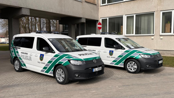 Attēlā pie administratīvās ēkas novietoti divi jauni Talsu novada Pašvaldības policijas operatīvie transportlīdzekļi – balti Volkswagen Caddy ar zaļi pelēku trafarējumu, uzrakstiem „Pašvaldības policija” un Talsu novada simboliku. Abiem transportlīdzekļiem uz jumta redzamas bākugunis.