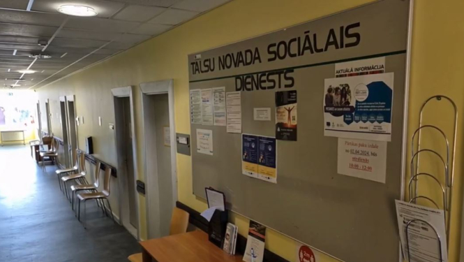 Talsu novada Sociālā dienesta gaitenis ar afišu dēli un krēsliem vienā gaiteņa pusē