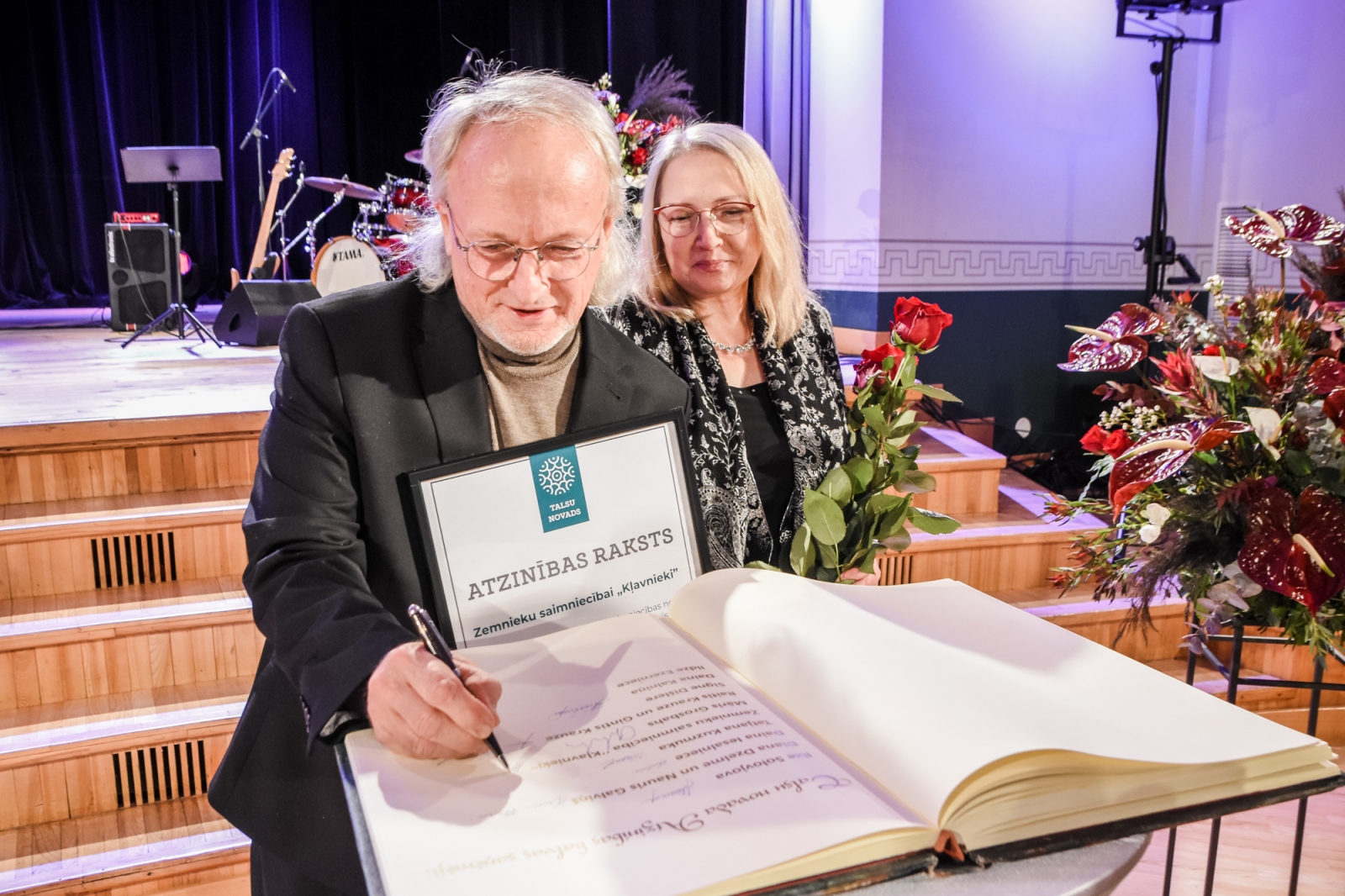 Ivars Šleiners parakstās Talsu novada Goda grāmatā, blakus Māra Šleinere (54)