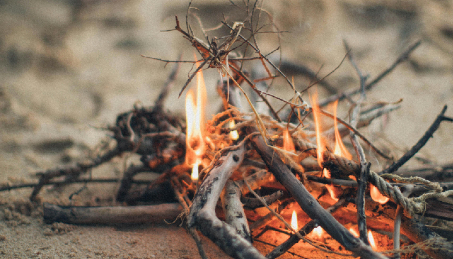 Neliels ugunskurs smiltīs no zariem un skaliem.